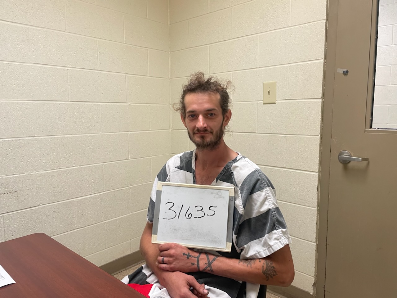 Person in striped uniform holding numbered sign in room.